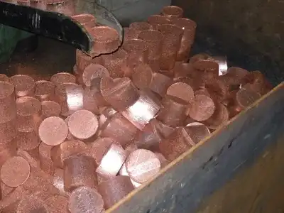 Cylindrical copper briquettes collected in a metal bin