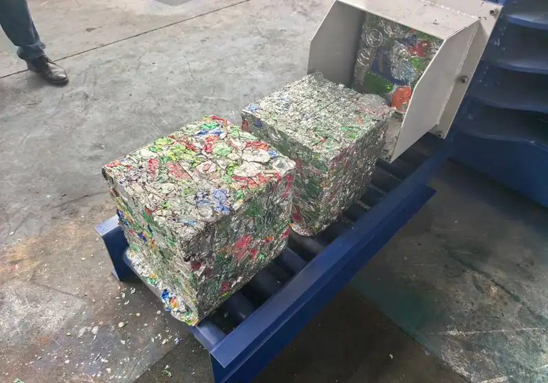 Compacted aluminium can bales emerging at the baler discharge outlet