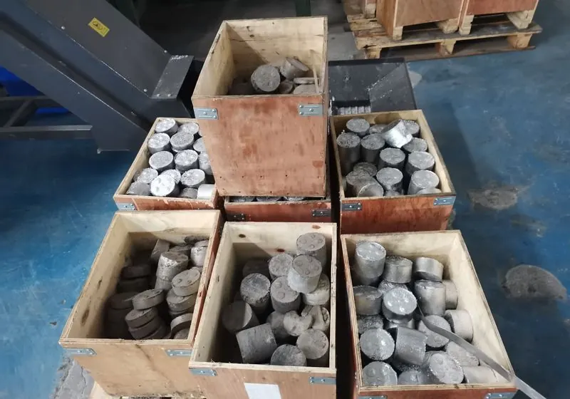 Cylindrical aluminium briquettes collected in wooden boxes beside processing equipment