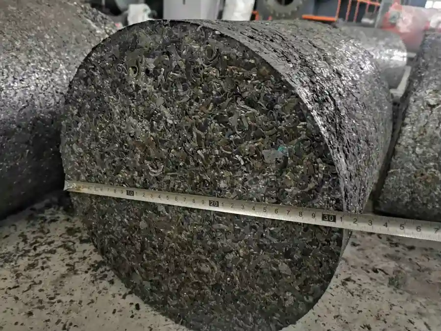 Large cylindrical iron chip briquette measured with a tape
